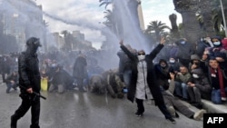 FILE: A Tunisian demonstrator flashes the V for victory sign as police fire water cannons during protests against President Kais Saied, on the 11th anniversary of the Tunisian revolution in the capital Tunis. Taken Jan. 14, 2022. -