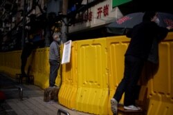 Residents wearing face masks pay for groceries by standing on chairs to peer over barriers set up to ring fence a wet market on a street in Wuhan, Hubei province, the epicenter of China's coronavirus disease (COVID-19) outbreak, April 1, 2020.