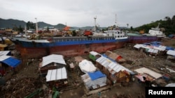FILE - Typhoon survivors living in temporary shelters are seen near ships that ran aground, nearly 100 days after super Typhoon Haiyan devastated Tacloban city in central Philippines.