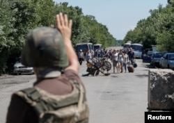 FILE - A member of the Ukrainian State Border Guard Service signals for people to stop as they approach a checkpoint at the contact line between Russia-backed rebels and Ukrainian troops, in Mayorsk, eastern Ukraine, July 3, 2019.