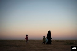 A woman walks with her children at a U.S.-backed Syrian Democratic Forces (SDF) screening area after being evacuated out of the last territory held by Islamic State militants, in the desert outside Baghuz, Syria, March 1, 2019.