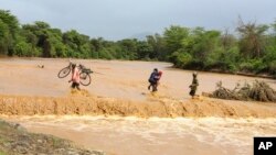 FILE — People are helped to cross a flooded Muuoni River, Makueni county, Nov. 24, 2023. 