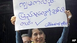 Burmese pro-democracy leader Aung San Suu Kyi displays a placard that reads, 'I also Love the People,' 14 Nov 2010။