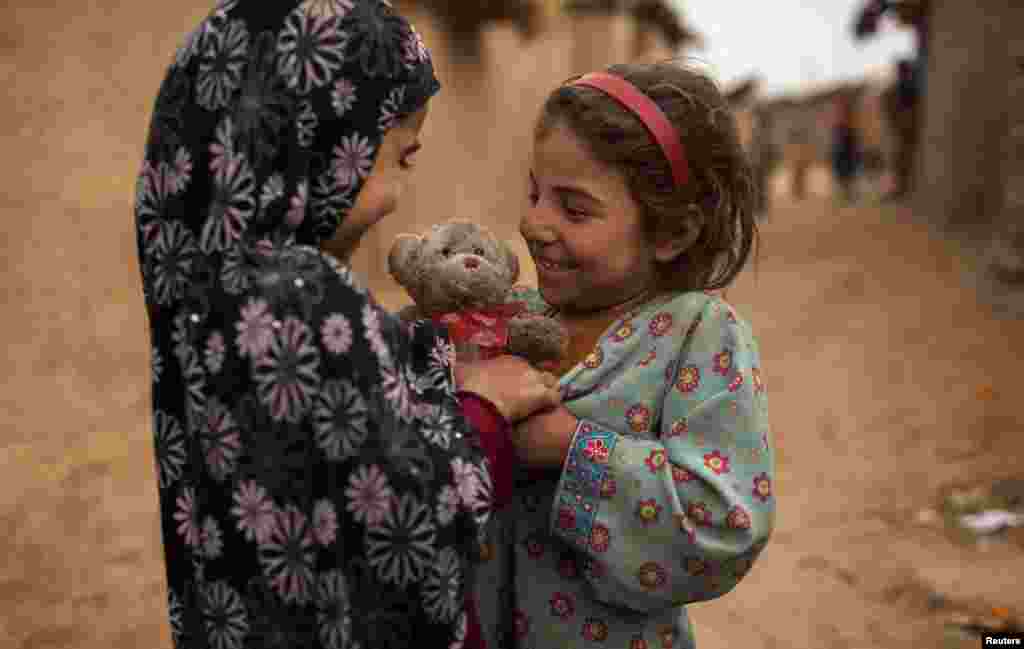 An Afghan refugee girl presents a stuffed toy with a heart-shaped ribbon to her friend on Valentine&#39;s Day in a slum on the outskirts of Islamabad, Pakistan.