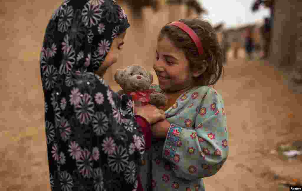An Afghan refugee girl presents a stuffed toy with a heart-shaped ribbon to her friend on Valentine's Day in a slum on the outskirts of Islamabad, Pakistan.