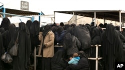 In this March 31, 2019, photo, women line up for aid supplies at Al-Hol camp in Hassakeh province, Syria. 