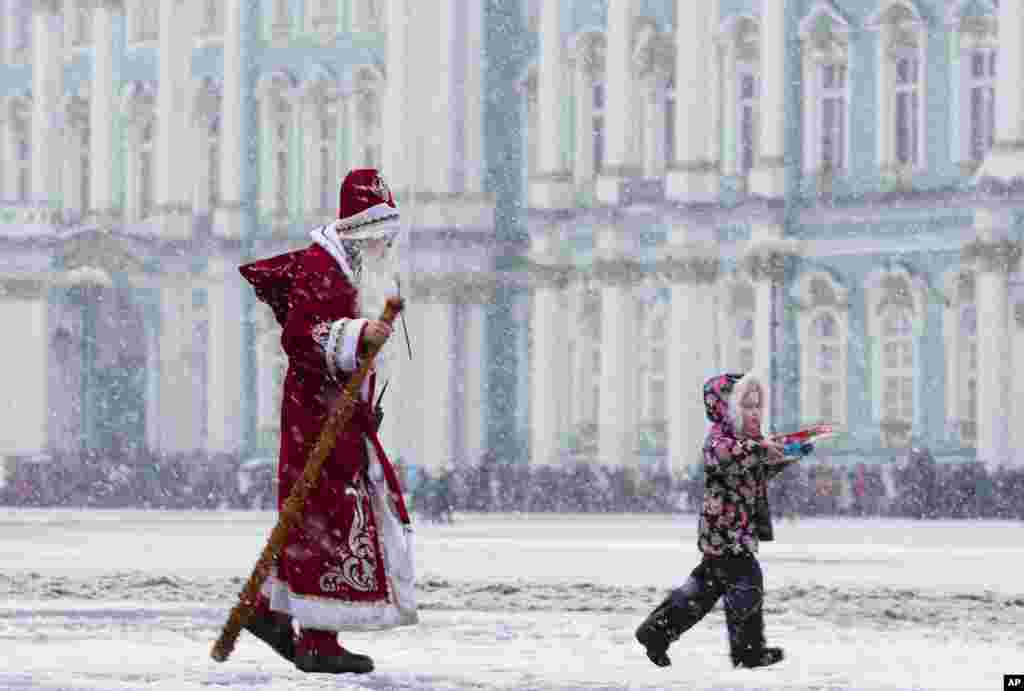 Seorang pria mengenakan kostum Ded Moroz (Grandfather Frost) berjalan di hujan salju di Lapangan Dvortsovaya di St. Petersburg, Rusia, 3 Januari 2015.