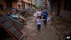 Una niña camina con su madre y su abuela por una calle con muebles amontonados y basura a los lados, en una zona afectada por las inundaciones en Paiporta, Valencia, España, el martes 5 de noviembre de 2024. 