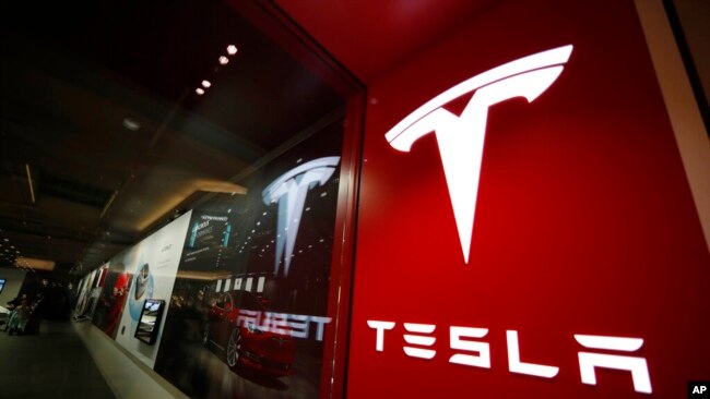 FILE- A sign bearing the company logo is displayed outside a Tesla store in Cherry Creek Mall in Denver, Feb. 9, 2019.
