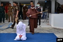 Perempuan pertama yang menjadi algojo hukum cambuk bersiap mencambuk seorang perempuan di Banda Aceh, 10 Desember 2019. (Foto: AFP)