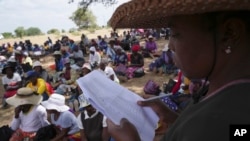 FILE - A woman reads out names of people waiting to receive food during a food distribution in Mangwe district southwestern Zimbabwe, amid a severe drought in Zimbabwe, March, 22, 2024. 
