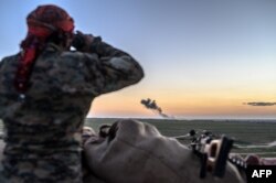 A Syrian Democratic Forces (SDF) fighter uses binoculars to inspect the embattled village of Baghuz, Syria, Feb. 19, 2019.