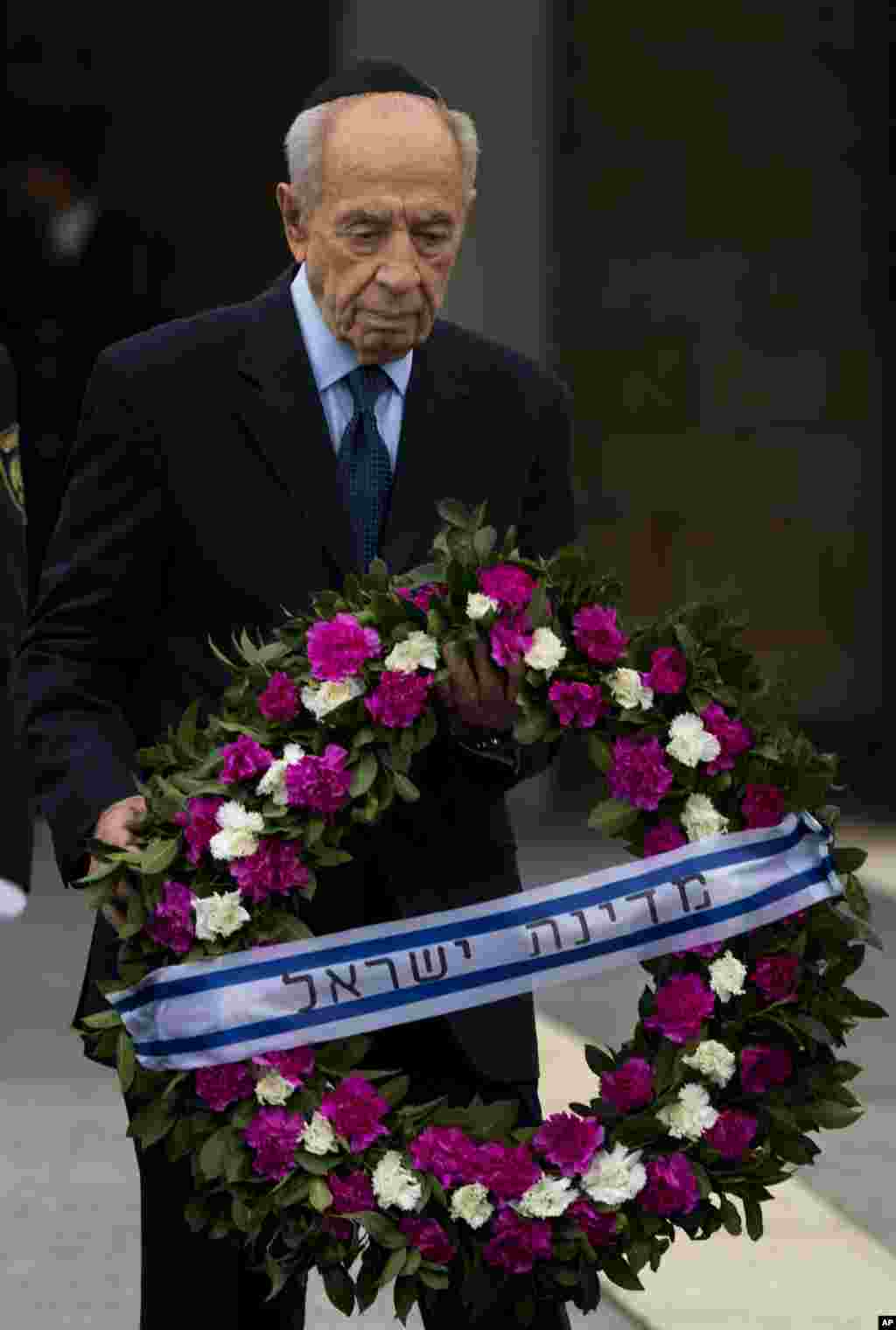 Presiden Israel Shimon Peres membawa karangan bunga untuk ditempatkan di peti jenazah Ariel Sharon di Knesset, kompleks parlemen Israel, Yerusalem (12/1). (AP/Bernat Armangue)