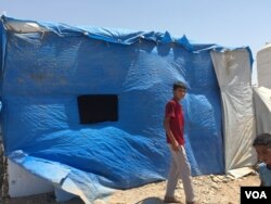 A displaced Sunni teenager walks past a blue plastic covered building in Baharka camp which houses just under 4,000 people on the outskirts of Irbil, in the Kurdistan region of Iraq, Aug, 2015. (VOA / S. Behn)