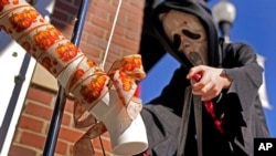 A boy gets candy via a plastic pipe to help prevent the spread of the new coronavirus as he trick-or-treats for Halloween, Oct. 31, 2020, in downtown Overland Park, Kan.