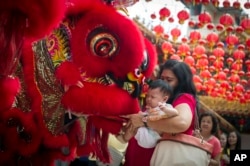 FILE - A Malaysian woman and her child give red packet to the lion dance troupe during the lion dance performance on the first day of Chinese Lunar New Year at a temple in Kuala Lumpur, Malaysia on Thursday, Feb. 19, 2015.
