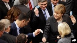 FILE - German Chancellor Angela Merkel, right, casts her vote at the German Federal Parliament in Berlin, Germany, Dec.4, 2015. 