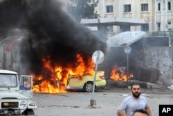 In this photo released by the Syrian official news agency SANA, Syrians gather in front of a burning car at the scene where suicide bombers blew themselves up, in the coastal town of Tartus, Syria, Monday, May 23, 2016.