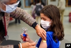 Jehna Kottori, 10, of Worcester, Mass., right, prepares to receive a shot of Pfizer COVID-19 vaccine, Dec. 2, 2021, at a mobile vaccination clinic, in Worcester.