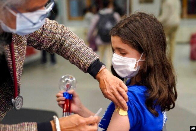 Jehna Kottori, 10, of Worcester, Mass., right, prepares to receive a shot of Pfizer COVID-19 vaccine, Dec. 2, 2021, at a mobile vaccination clinic, in Worcester.