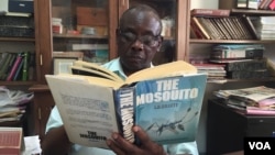 Louis Mukwaya, mosquito researcher at the Uganda Virus Research Institute near Entebbe, reads at his desk about his primary subject of study. (J. Craig/VOA) 