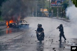 A police officer aims his shotgun at two men riding a motorcycle during a protest against Nicaragua's President Daniel Ortega in Managua, May 28, 2018.
