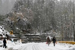 Orang-orang berjalan di jalan yang tertutup salju saat salju turun di Murree, sekitar 65 km utara Islamabad pada 12 Desember 2020. (Foto: AFP/Aamir Qureshi)