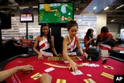 FILE - Attendants conduct play with the visitors over a Black Jack gaming table during the Global Gaming Expo Asia in Macau.