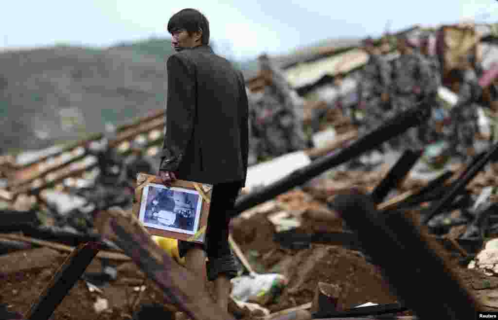 A man carries a picture as he stands among debris in the Longtoushan township of Ludian county, Yunnan province, Aug. 4, 2014