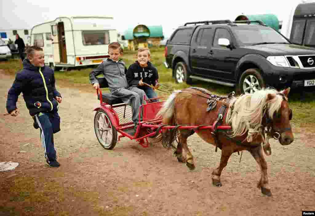 Wisatawan mengendarai sebuah kereta kuda melintasi tempat perkemahan di Westmorland, Inggris. Para wisatawan mengunjungi kota ini sebagai bagian dari pameran kuda tahunan yang menjadi tradisi kota ini sejak abad ke-17.