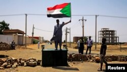 A Sudanese protester holds a national flag as he stands on a barricade along a street, demanding that the country's Transitional Military Council hand over power to civilians, in Khartoum, Sudan, June 5, 2019.