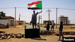 A Sudanese protester holds a national flag as he stands on a barricade along a street, demanding that the country's Transitional Military Council hand over power to civilians, in Khartoum, Sudan, June 5, 2019.
