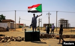 FILE - A Sudanese protester holds a national flag as he stands on a barricade along a street, demanding that the country's Transitional Military Council hand over power to civilians, in Khartoum, Sudan, June 5, 2019.