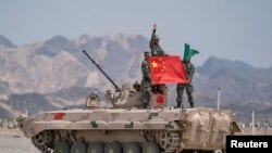 Tentara China dari Tentara Pembebasan Rakyat (PLA) berpose untuk foto dengan bendera nasional China di sebuah tank di Korla, Daerah Otonomi Uighur Xinjiang. (Foto: Reuters)