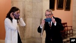 Dr. Amy Acton, left, director of the Ohio Department of Health, and Ohio Gov. Mike DeWine put on their homemade masks following a news conference on the state's response to the ongoing COVID-19 pandemic, April 6, 2020, at the Ohio Statehouse in Columbus.