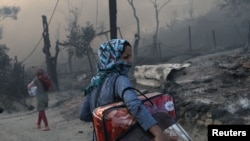 A migrant carries her belongings following a fire at the Moria camp for refugees and migrants on the island of Lesbos, Greece, Sept. 9, 2020. 