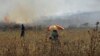 A Palestinian protester sits as a burning farm is seen during clashes with Israeli troops following the killing of an 18-month-old Palestinian toddler, at the Israeli Hawara checkpoint near the West Bank city of Nablus, July 31, 2015.