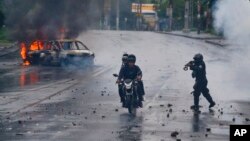 FILE - A police officer aims his shotgun at two men riding a motorcycle during a protest against Nicaragua's President Daniel Ortega in Managua, Nicaragua, May 28, 2018. 