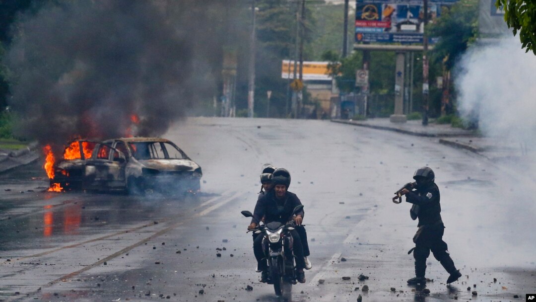 Seorang polisi mengarahkan senjatanya ke dua pria yang menaiki motor dalam unjuk rasa terhadap Presiden Nikaragua Daniel Ortega di Magua, Nikaragua, 28 Mei 2018.
