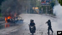 Seorang polisi mengarahkan senjatanya ke dua pria yang menaiki motor dalam unjuk rasa terhadap Presiden Nikaragua Daniel Ortega di Magua, Nikaragua, 28 Mei 2018.
