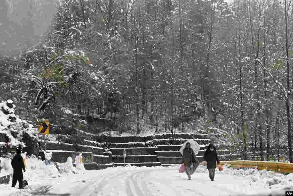 Orang-orang berjalan di jalan yang tertutup salju saat turun salju di Murree, sekitar 65 km di utara Islamabad. (Foto: Aamir QURESHI / AFP)