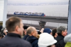 People watch a giant TV screen with Russian President Vladimir Putin, inside, riding a train across a bridge linking Russia and the Crimean peninsula in Taman, Russia, Dec. 23, 2019.
