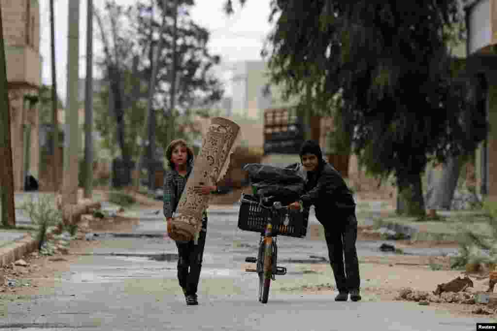 A boy pushes a bicycle as another one carries a carpet along a deserted street in Aleppo's al-Sakhour district, Syria.