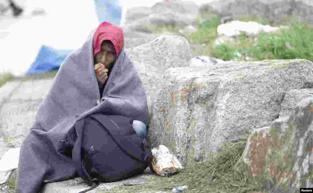 Seorang migran memakai selimut sambil makan apel di kamp darurat di tempat penyeberangan perbatasan di Nickelsdorf, Austria (6/9). ​(Reuters/Srdjan Zivulovic)