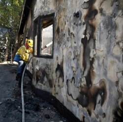 A firefighter douses water on a house after it was burned by the wind-driven Getty Fire in West Los Angeles, California, Oct. 28, 2019.