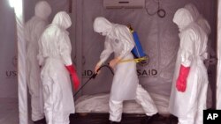 Health workers wearing protective gear spray the shrouded body of a man with disinfectant as they suspect he died from the Ebola virus, at a USAID, American aid Ebola treatment center at Tubmanburg on the outskirts of Monrovia, Liberia, Nov. 28, 2014.