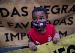 A black boy wearing a mask against the spread of the new coronavirus, holds a sign during a protest against racism and police violence in a "Black Lives Matter" demonstration in Duque de Caxias, Brazil, June 10, 2020.
