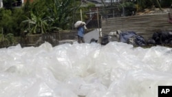 An Indonesian man carries used plastics to be sold to a recycling center, as he walks in front of discarded plastic bags, in Jakarta, Indonesia, Thursday, Dec 6, 2007. Delegates from 190 nations have assembled on the resort island of Bali, Indonesia…