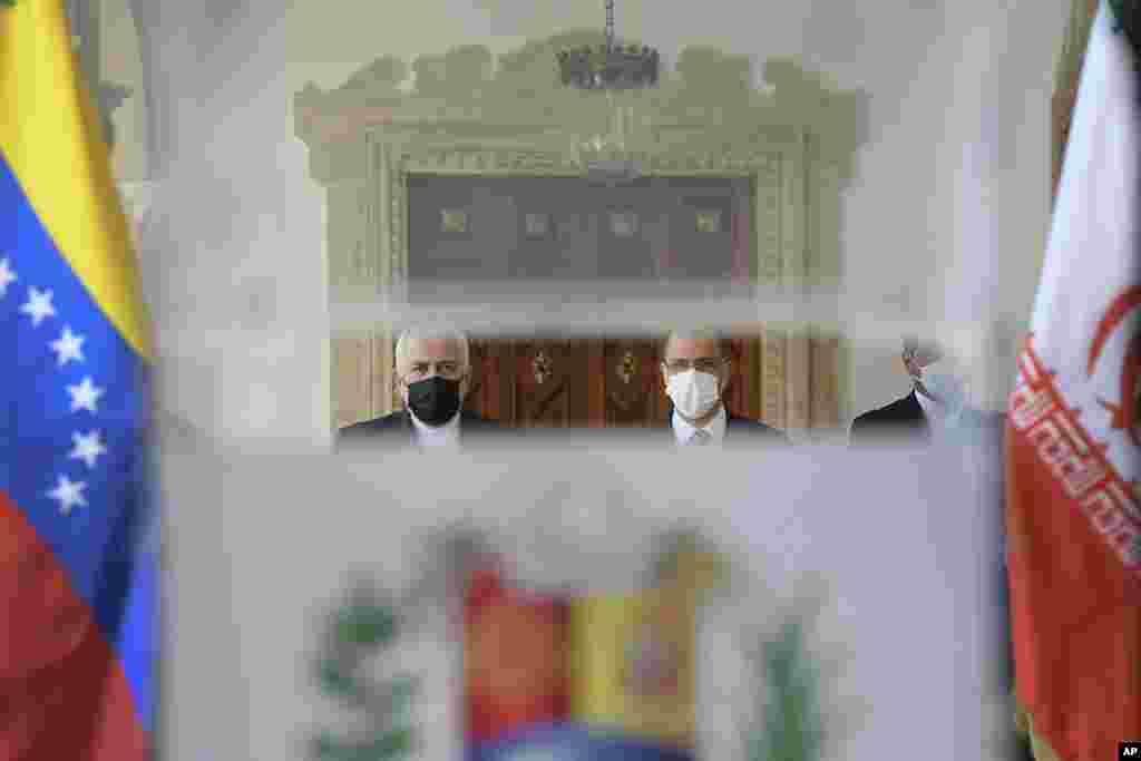 Seen through a translucent podium, Iran's Foreign Minister Mohammad Javad Zarif, left, and Venezuela's Foreign Minister Jorge Arreaza, right, arrive to give a press conference at the Foreign Ministry in Caracas, Venezuela, Thursday, Nov. 5, 2020, amid the