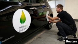 FILE - An employee installs a sticker which reads 100% electric next to the logo of the upcoming COP21 Climate Change Conference on a Nissan LEAF electric car in Boulogne-Billancourt, near Paris, France, November 16, 2015.
